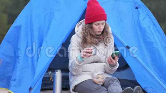 漂亮的女游客戴着红帽子坐在旅游帐篷里喝着热水瓶里的茶视频的预览图