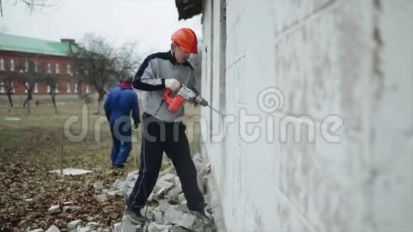 一个人用射孔器打破外面的墙戴防护头盔的人拆除工作视频的预览图