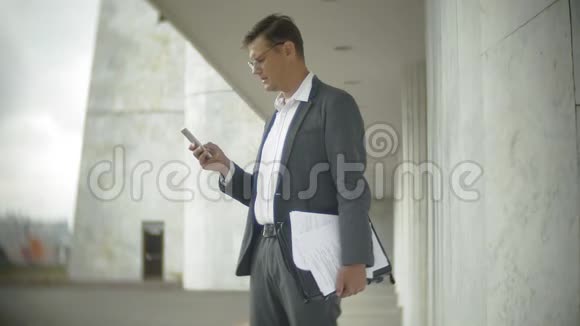 城里的商人他穿着西装和公文包他翻阅文件在智能手机上交谈视频的预览图