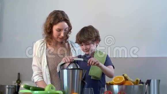 年轻的白种人母亲和孩子在厨房用电榨汁机制作鲜橙果汁视频的预览图