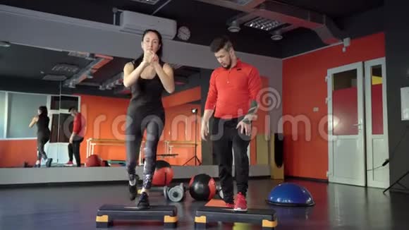 在健身房里一个年轻健康运动活跃的身材女孩旁边有一位英俊乐于助人的私人教练视频的预览图