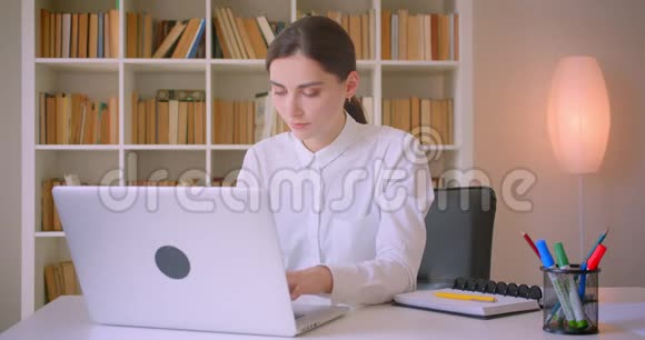 在办公室室内使用笔记本电脑的年轻有魅力的高加索女商人的特写肖像视频的预览图