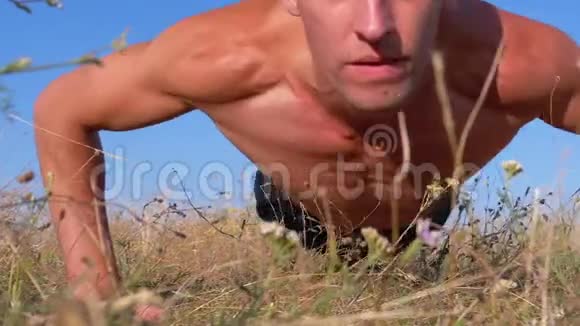 裸露躯干的年轻运动员在大自然中做俯卧撑视频的预览图
