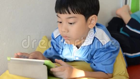 小亚洲男孩微笑着在脸上玩平板电脑视频的预览图