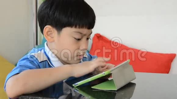 小亚洲男孩微笑着在脸上玩平板电脑视频的预览图