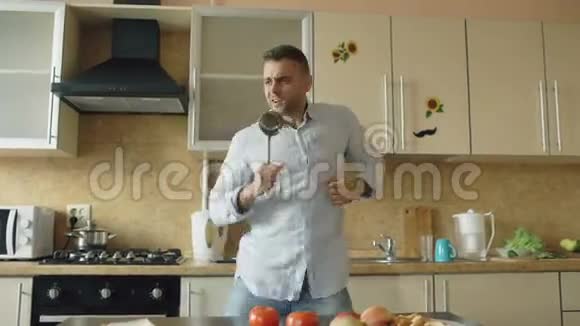 有魅力的年轻风趣男子在家厨房做饭时用瓢泼大雨跳舞唱歌视频的预览图