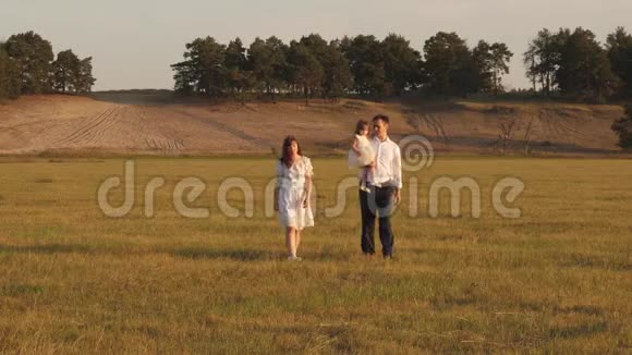 爸爸和小女儿妈妈在阳光下的田野里散步孩子爸爸和妈妈在阳光下的草地上玩耍视频的预览图