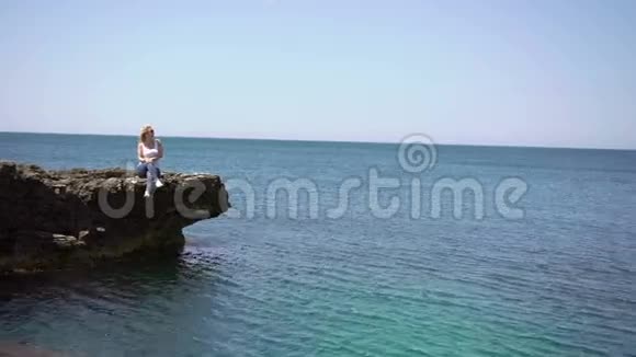 在海边的岩石上年轻的金发女郎视频的预览图