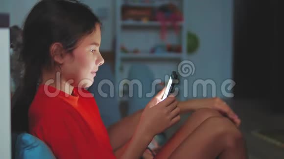 有智能手机的小女孩躺在床上睡觉在家里上网玩智能手机网络游戏的小女孩视频的预览图