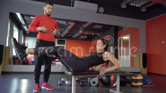 在健身房里一个年轻健康运动活跃的身材女孩旁边有一位英俊乐于助人的私人教练视频的预览图