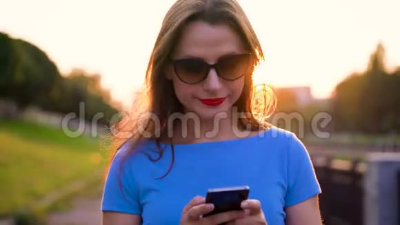 日落时分戴太阳镜的女人在户外使用智能手机视频的预览图
