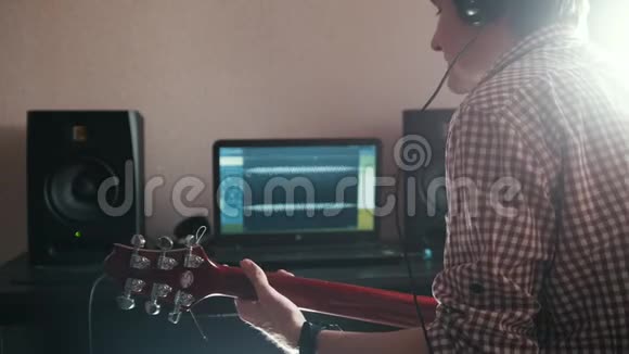 年轻的男音乐家用电脑耳机和键盘作曲并录制弹吉他的配乐视频的预览图