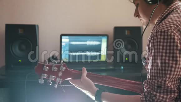 年轻音乐家用电脑耳机和键盘作曲并记录弹吉他的配乐视频的预览图