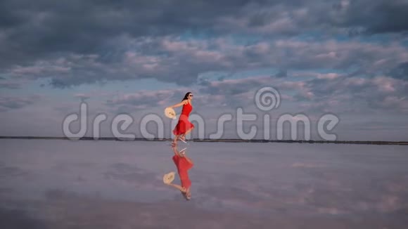 穿着飘舞裙的女孩沿着一个盐湖奔跑云彩反射在水中视频的预览图