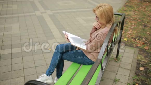金碧辉煌的女子读书书在秋天的公园里视频的预览图