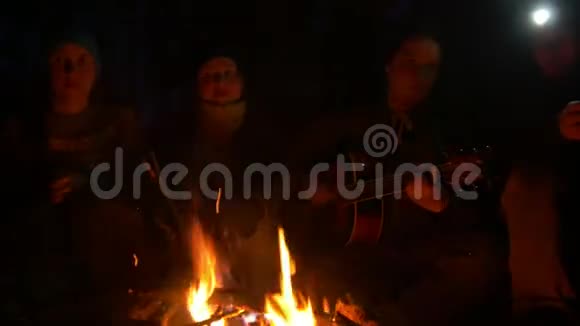晚上森林里坐在篝火旁弹吉他的年轻朋友视频的预览图