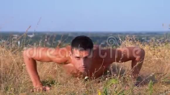 裸露躯干的年轻运动员在大自然中做俯卧撑视频的预览图