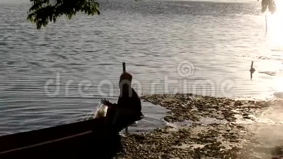 男孩靠船在湖里当渔夫谋生剪影视频的预览图
