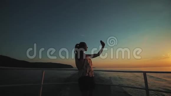 一个美丽迷人的女孩正在摆姿势在背景下拍摄日落时的自拍视频的预览图