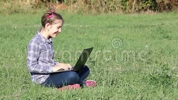 小女孩坐在草地上玩手提电脑视频的预览图