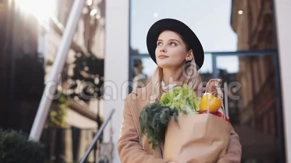 穿着时尚外套的年轻美女拿着一包产品走在街上微笑着视频的预览图