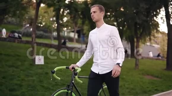 白人青年穿着白色衬衫骑着自行车在城里的街道上行走边走边骑着他的徒步自行车视频的预览图