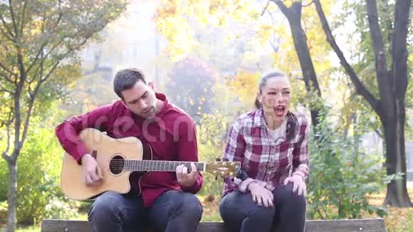 男人一边弹吉他一边和女人一起唱歌一边坐在公园的长椅上视频的预览图