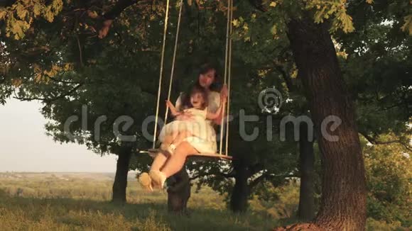 母亲和婴儿在森林中的橡树枝上骑着一条绳秋千妈妈摇着女儿在阳光下摇摆视频的预览图