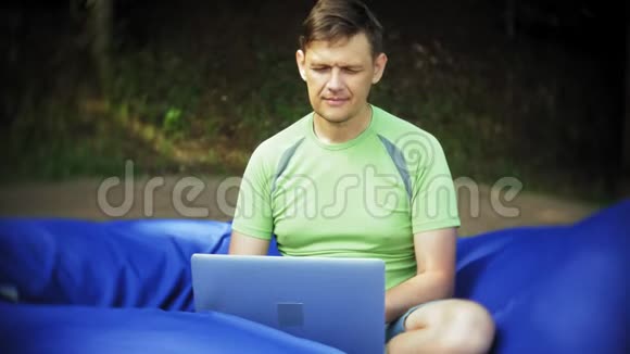 成熟的男人使用笔记本电脑躺在公园的休息区软泡芙上视频的预览图