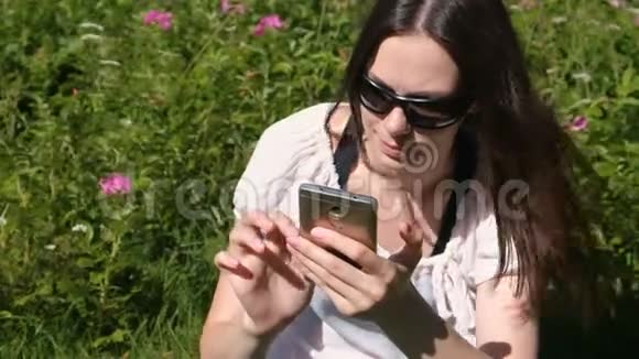 在阳光明媚的日子里坐在公园里的女人正在用手机输入一条信息视频的预览图