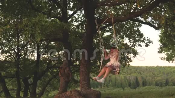 十几岁的女孩喜欢在森林里度过一个夏天的秋千上飞行快乐的女孩在橡树上摇摆着绳子视频的预览图