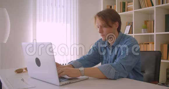 年轻有魅力的高加索商人在办公室室内使用笔记本电脑的特写照片视频的预览图
