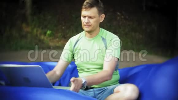 成熟的男人使用笔记本电脑躺在公园的休息区软泡芙上视频的预览图
