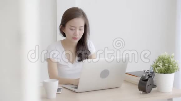 美丽的年轻自由职业亚洲女性微笑着在办公桌办公室的笔记本电脑上工作和打字视频的预览图