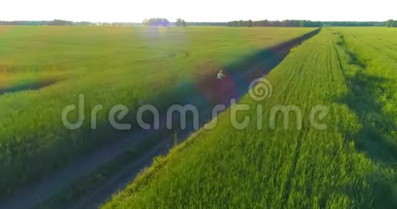 鸟瞰年轻男孩骑着自行车穿过古老的乡村道路上的麦田阳光和光束视频的预览图