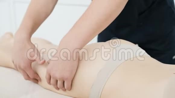 一位男性理疗师做一次轻按摩以暖和一位年轻女性的臀部和臀部视频的预览图