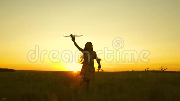 快乐的女孩带着玩具飞机在夕阳下的田野上奔跑孩子们玩玩具飞机青少年的梦想视频的预览图