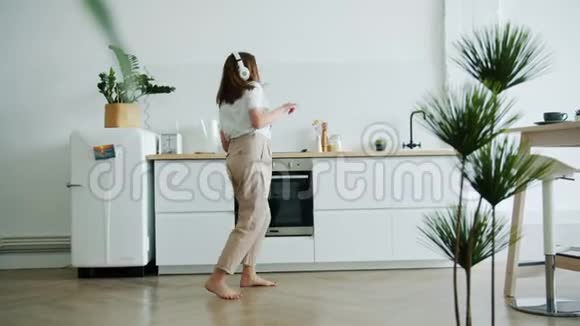 快乐的年轻女子在家里用耳机听音乐跳舞视频的预览图