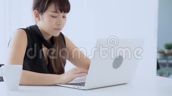 美丽的年轻自由职业亚洲女性微笑着在办公桌办公室的笔记本电脑上工作和打字视频的预览图
