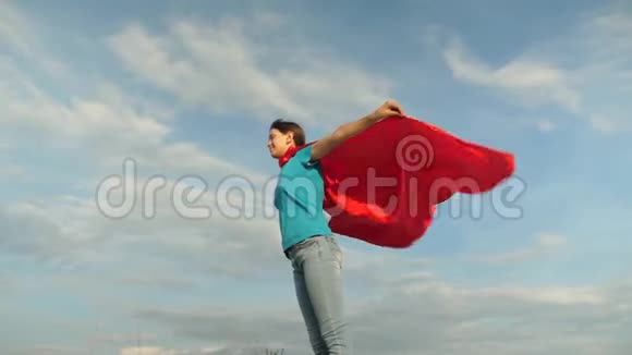美丽的女孩超级英雄穿着红色斗篷站在田野上斗篷随风飘扬慢动作女孩的梦想视频的预览图