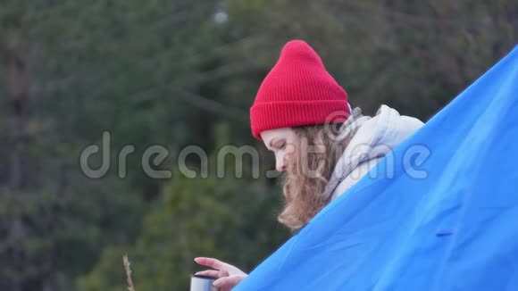 漂亮的女游客戴着红帽子坐在旅游帐篷里喝着热水瓶里的茶视频的预览图