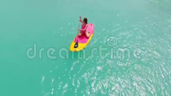 在蓝色海洋中站立桨板上的女人的空中视野视频的预览图