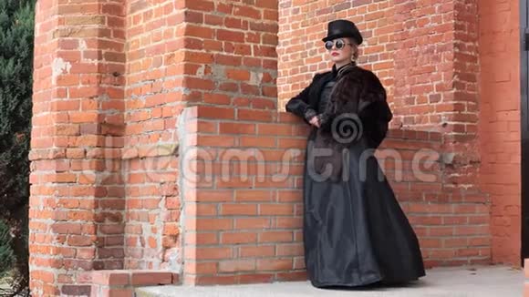 秋天穿着黑色裙子的女孩在砖墙的背景下视频的预览图