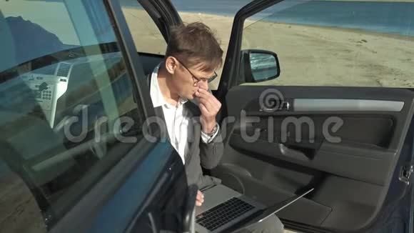 一个拿着笔记本电脑手提箱的商人在他的汽车附近的海滩上放松视频的预览图