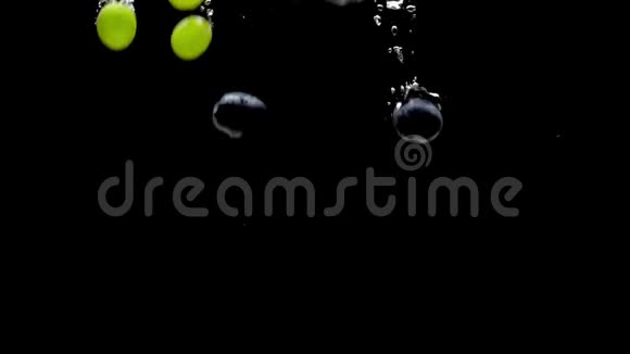 绿色和蓝色的葡萄落在透明的水中黑色的背景视频的预览图