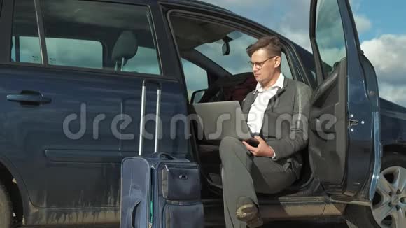 一个拿着笔记本电脑手提箱的商人在他的汽车附近的海滩上放松视频的预览图