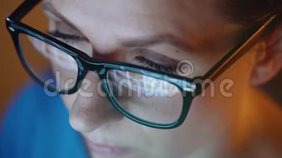 戴眼镜的女人看着显示器和上网监视器屏幕反映在眼镜上视频的预览图