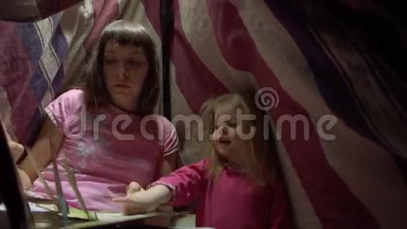 妈妈和孩子女儿晚上在帐篷里看一本带手电筒的书视频的预览图
