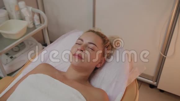美丽的年轻女性穿着浴袍躺在豪华水疗沙龙等待面部护理程序视频的预览图
