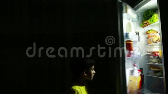 孩子半夜在冰箱前吃零食饥饿的男孩视频的预览图